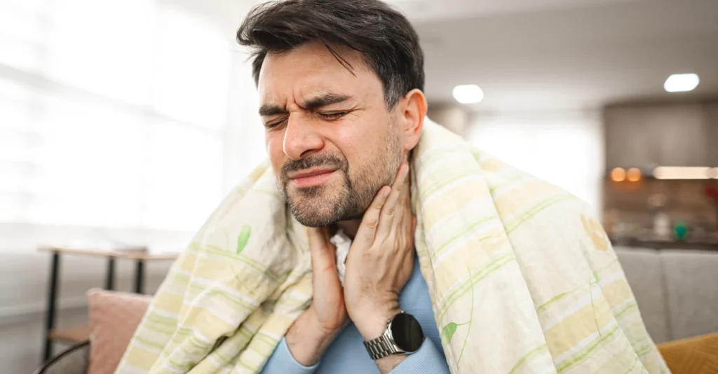 sick-man-covered-with-blanket-is-sitting-holding-his-sick-throat