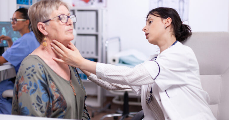 A doctor performs a physical examination of a patient's neck and throat in a clinical setting.